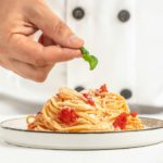 Chef preparing delicious pasta tomatoes and basil on a light background. Italian cuisine