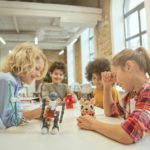 Development. Joyful diverse children sitting at the table, looking at technical toys full of details