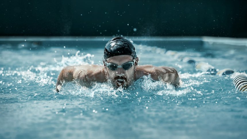 dynamic and fit swimmer in cap breathing performing the butterfly stroke